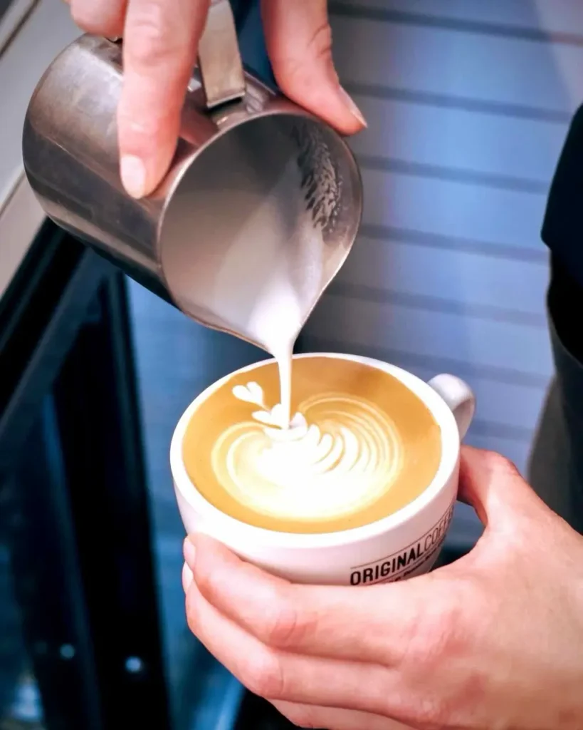 The barista pouring milk to a cup of original coffee